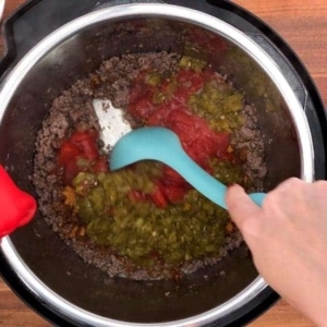 stirring the ingredients for taco pasta into the ground beef