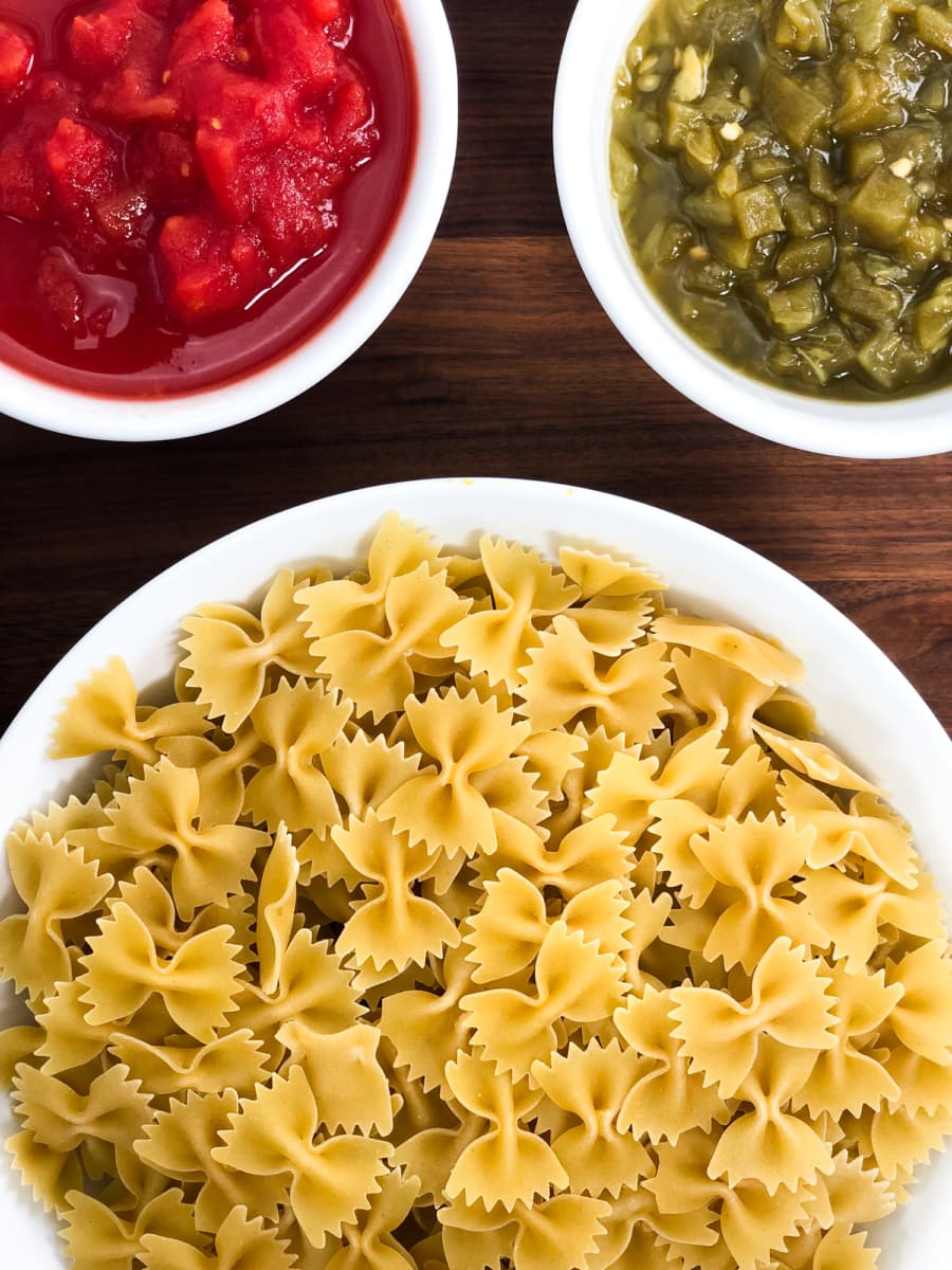 ingredients for taco pasta including a bowl of farfalle pasta, a bowl of fire-roasted tomatoes, and a bowl of diced chiles