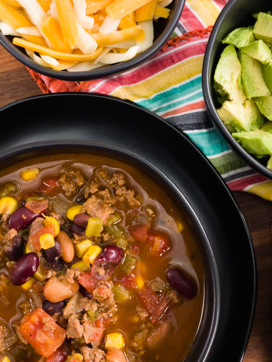 a bowl of taco soup served with shredded cheese and avocado