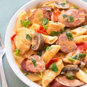 a bowl of creamy cajun pasta with sausage garnished with cilantro