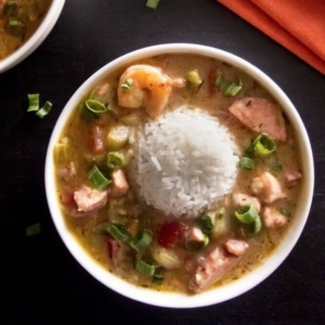 a bowl of gumbo garnished with scallions with a ball of rice in the center