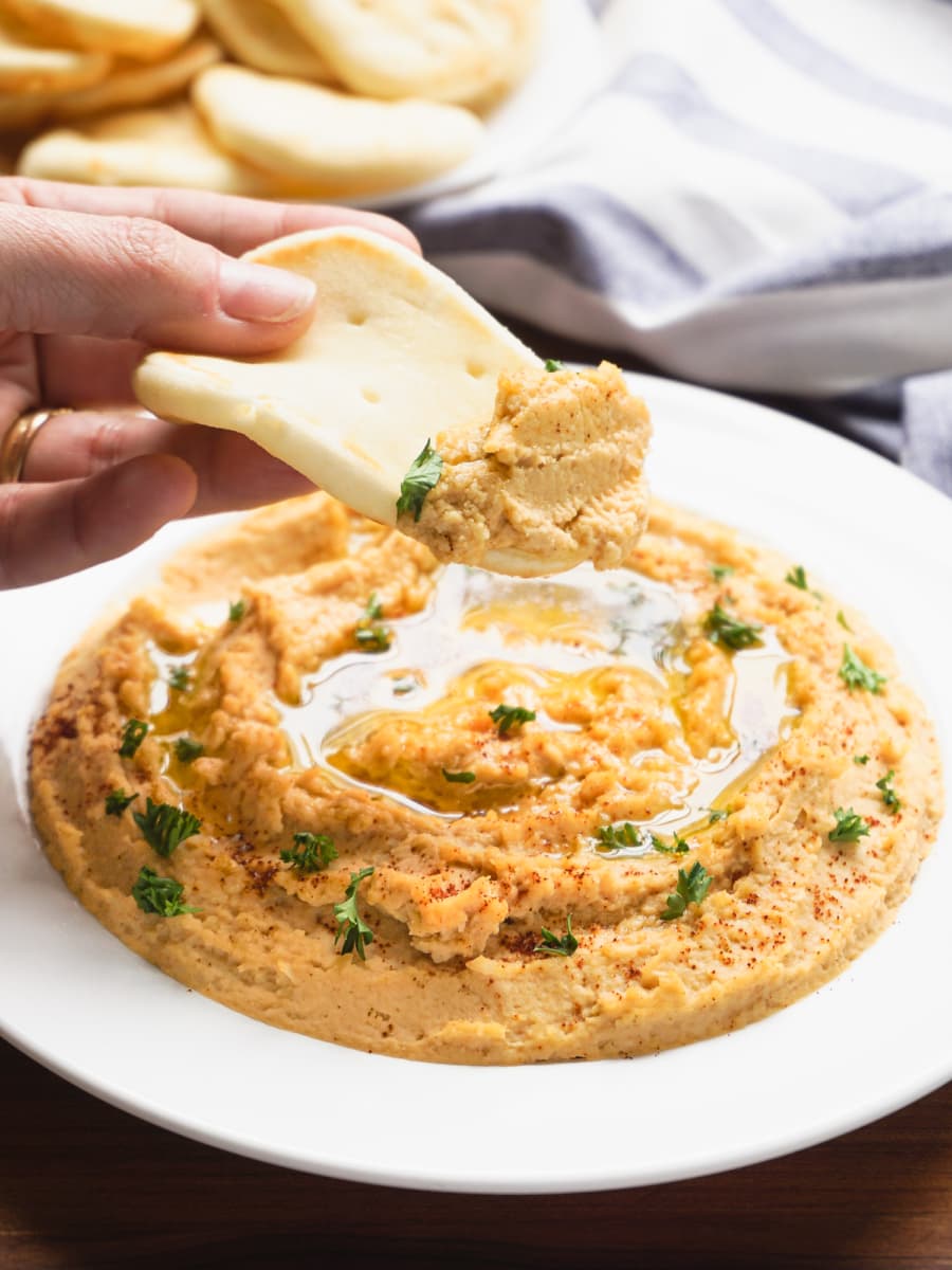 homemade hummus on a plate being dipped with bread