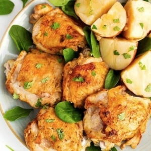 overhead shot of chicken thighs and potatoes garnished with basil leaves