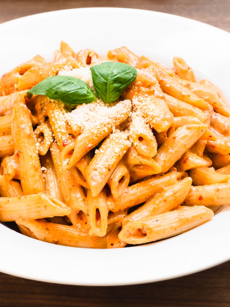 creamy sun dried tomato pasta in a bowl topped with parmesan and garnished with basil