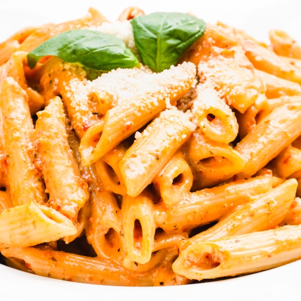 a bowl of creamy sun-dried tomato pasta topped with parmesan and basil leaves