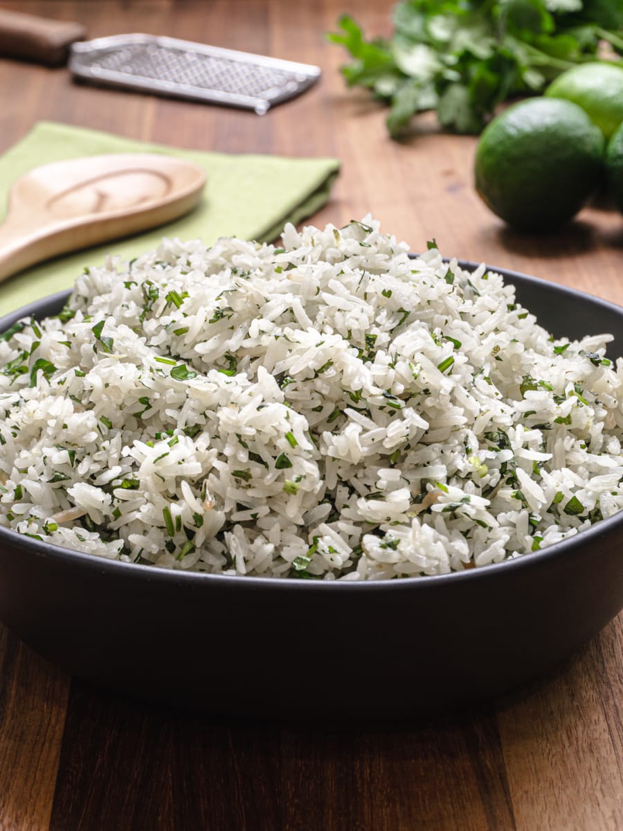 a bowl of cilantro lime rice sitting on a wood countertop with limes and cilantro in the background