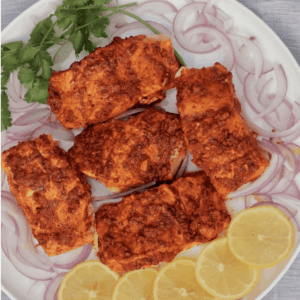 tandoori salmon on a plate garnished with lemon slices and cilantro