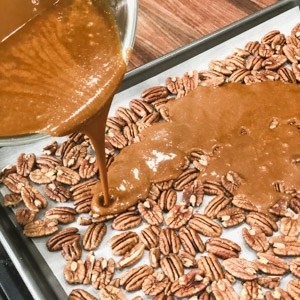 pouring toffee over pecans on a baking sheet