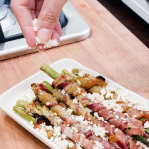 sprinkling crumbled feta over bacon wrapped asparagus