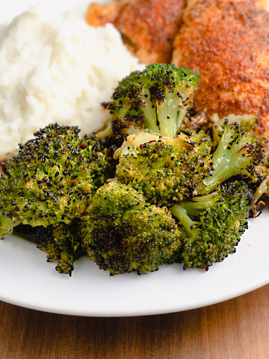 oven roasted broccoli served on a plate with mashed potatoes and chicken