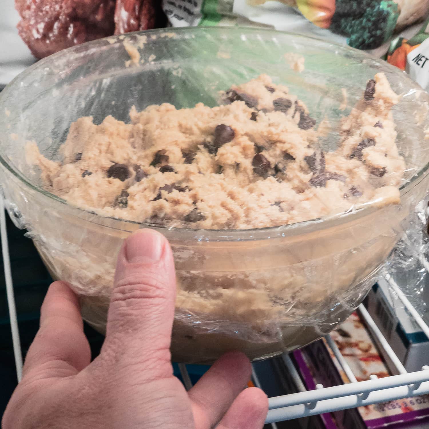 placing a covered bowl of chocolate chip cookie dough in the freezer