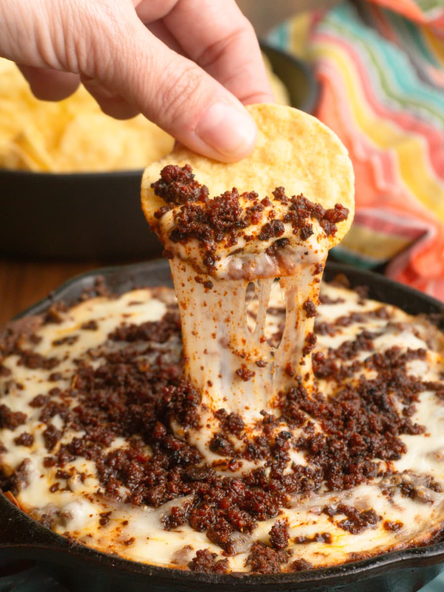 dipping a tortilla chip into an anafre hondureno chorizo bean and cheese dip