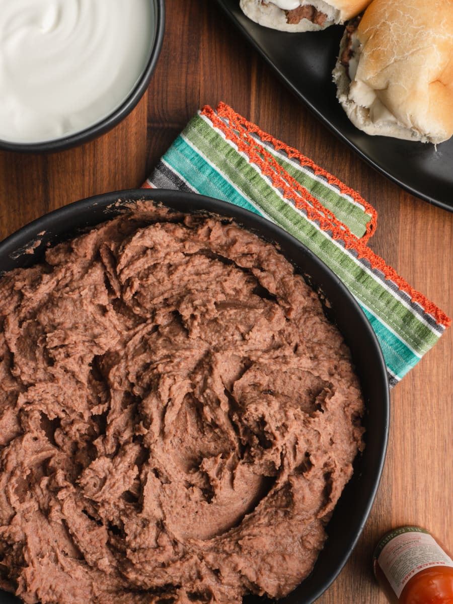 a large serving bowl of authentic refried beans served with a small bowl of crema