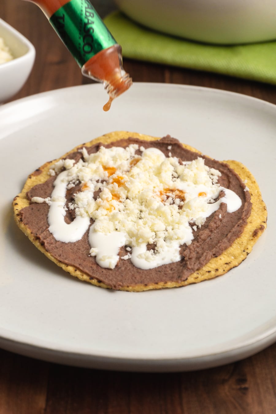  a tostada or toasted tortilla with refried beans and hot sauce being dipped over it