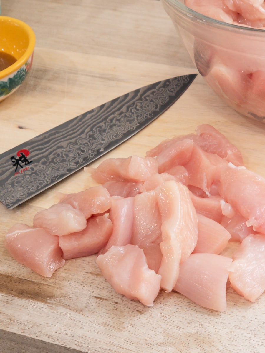 a pile of chicken cut into bite-sized pieces on a cutting board next to a knife