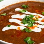 a bowl of bean soup garnished with cilantro drizzled with mantequilla and hot sauce