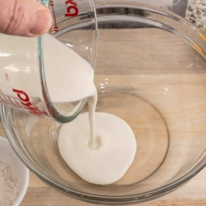 pouring heavy cream in a mixing bowl to make homemade alfredo sauce