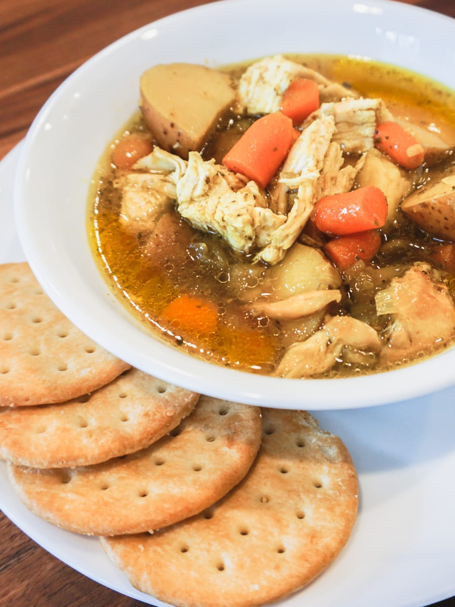 Delicious bowl of Instant Pot Chicken soup with potatoes, carrots, chicken, and crackers on the side.