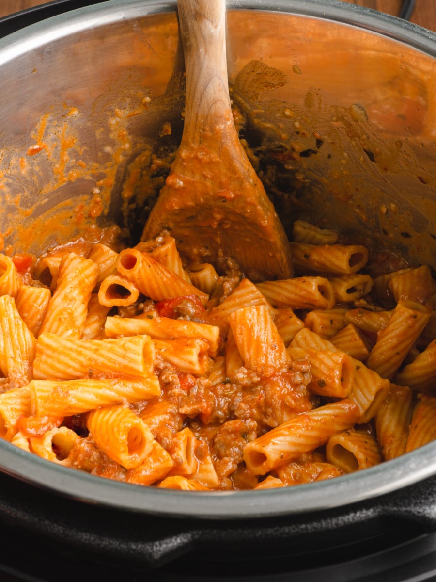 freshly made pot of instant pot creamy sausage rigatoni being mixed with a wooden spoon