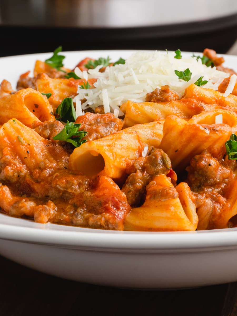 a close up of a bowl of instant pot creamy sausage rigatoni topped with shredded parmesan and parsley