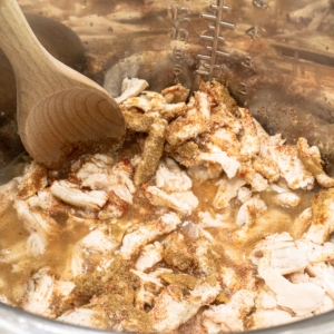 mixing shredded chicken and spices into chicken stock in the instant pot using a wooden spoon