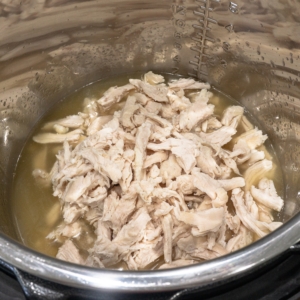 shredded chicken sitting in chicken stock in the instant pot for making white chicken chili