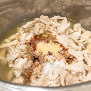 shredded chicken with spices sitting in chicken stock in the instant pot for white chicken chili