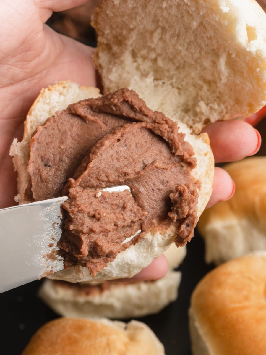 spreading authentic refried beans on a small roll to make pan con frijoles