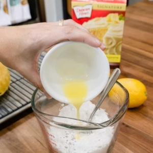 adding melted butter to a measuring cup with confectioners sugar, and lemon juice to make a lemon glaze