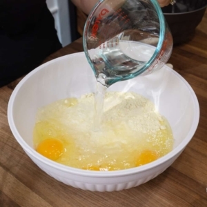 pouring water into a mixing bowl with lemon cake mix and cracked raw eggs