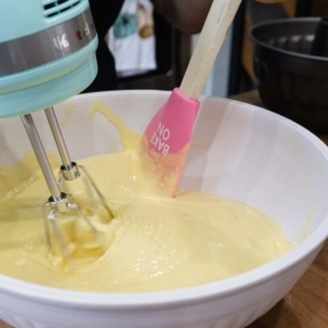 using a handmixer for mixing a lemon cake batter and a spatula for scraping down the sides of the bowl