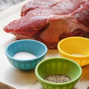 a large chuck roast and seasoning including kosher salt, pepper, and garlic powder