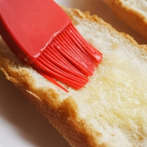 brushing melted butter on french bread