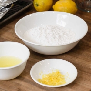 bowls filled with the ingredients for making a lemon glaze including confectioners sugar, lemon juice, and lemon zest