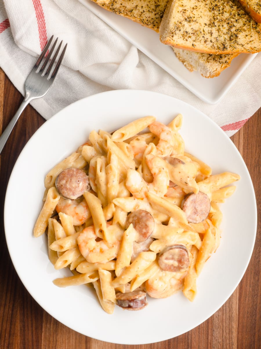 view from above of a bowl of instant pot creamy cajun shrimp alfredo with sausage and garlic bread on the side