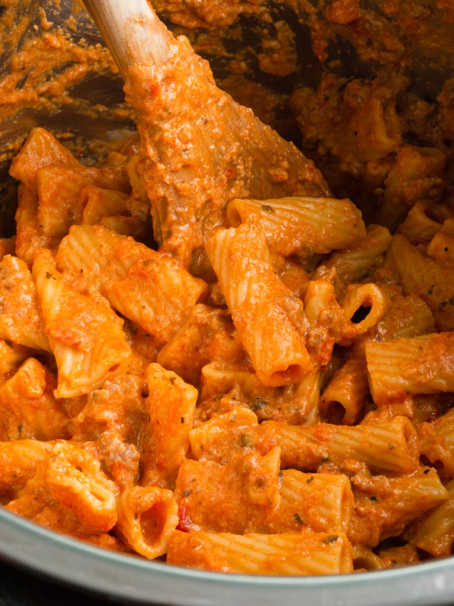 a wooden spoon stirring cheesy sausage rigatoni inside an instant pot pressure cooker