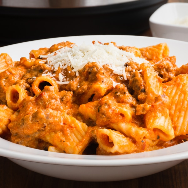 a white bowl with instant pot cheesy sausage rigatoni topped with parmesan cheese