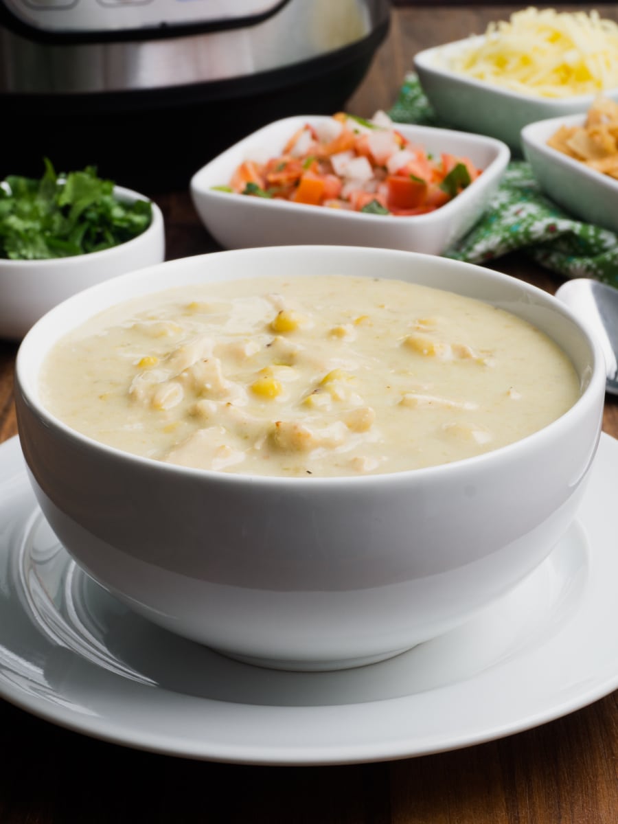 a bowl of instant pot chicken enchilada soup with cilantro, pico, and cheese in the background