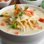 a bowl of homemade enchilada soup topped with pico de gallo, shredded cheese, and fried tortilla strips