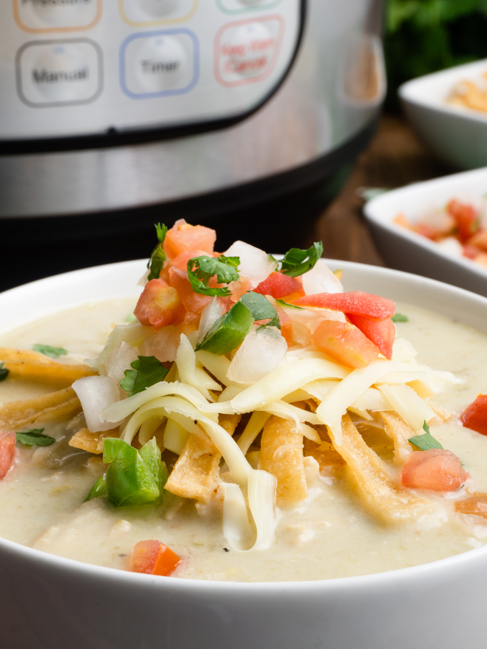 a bowl fo instant pot chicken enchilada soup topped with fried tortilla strips, shredded cheese, and pico de gallo