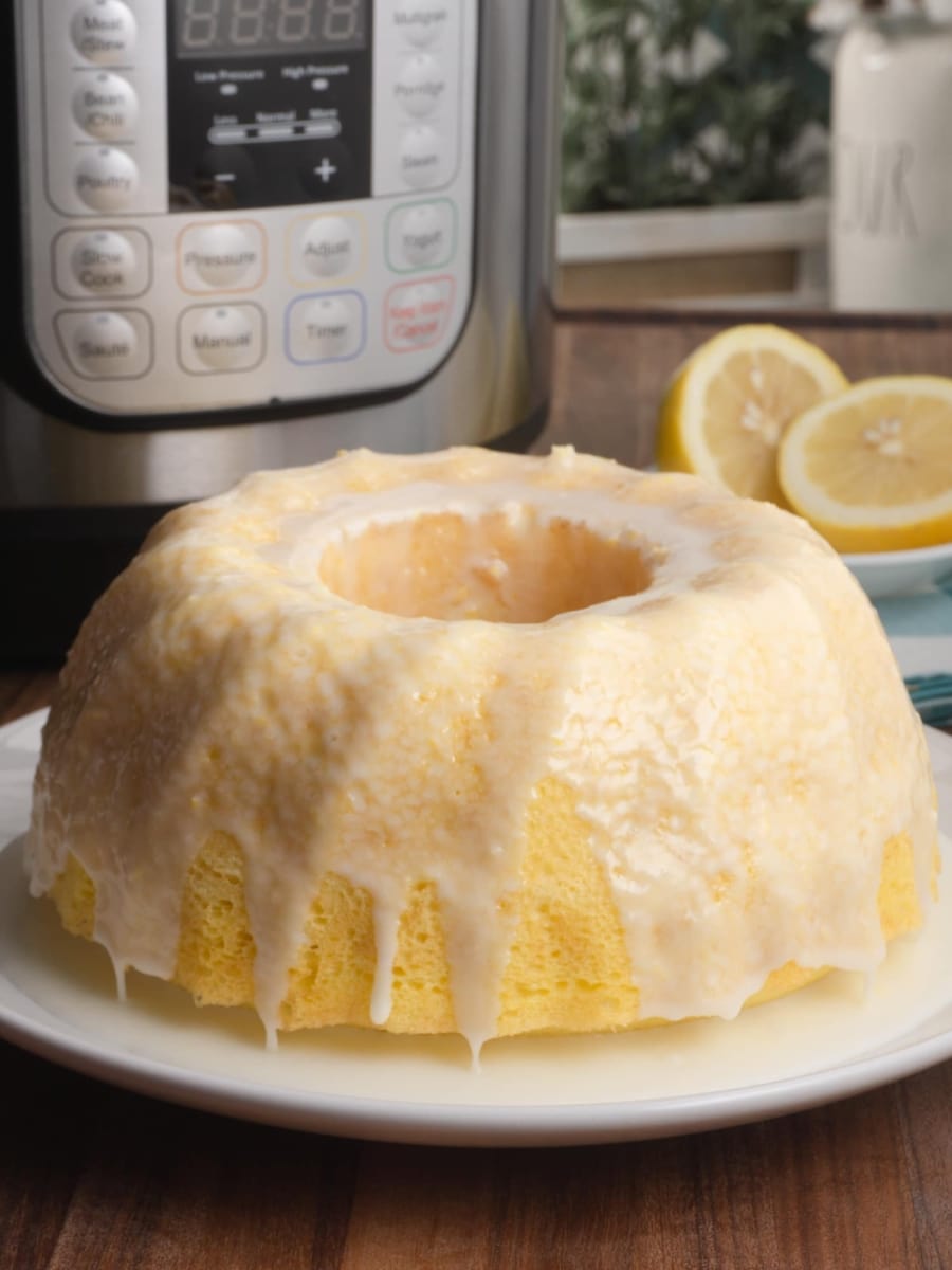 a beautiful instant pot lemon bundt cake with lemon glaze on top and the instant pot and lemons in the background