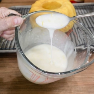 a spoonful of lemon glaze made in a measuring cup using powdered sugar, lemon juice, lemon zest, and butter