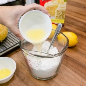 pouring freshly squeezed lemon juice into a measuring cup with confectioners sugar