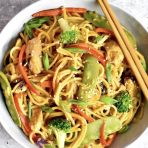 overhead shot of chicken lo mein in a bowl garnished with sesame seeds