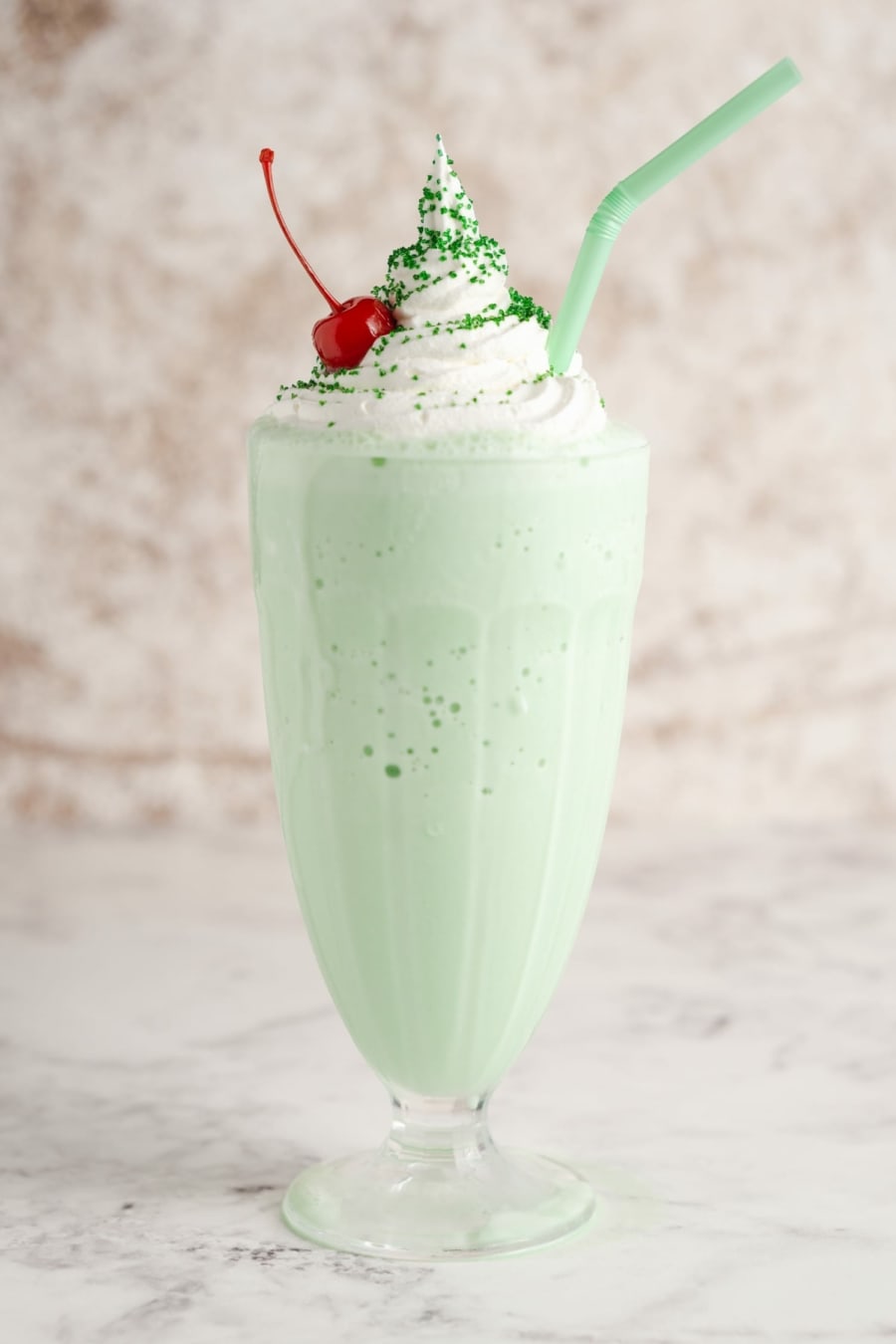 a shamrock shake in a milk shake glass topped with whipped cream and a cherry