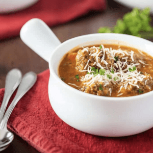 meatball soup garnished with cilantro and shredded cheese served in a soup bowl