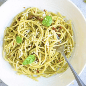 overhead shot of a bowl of spaghetti in pesto sauce garnished with basil and shredded cheese