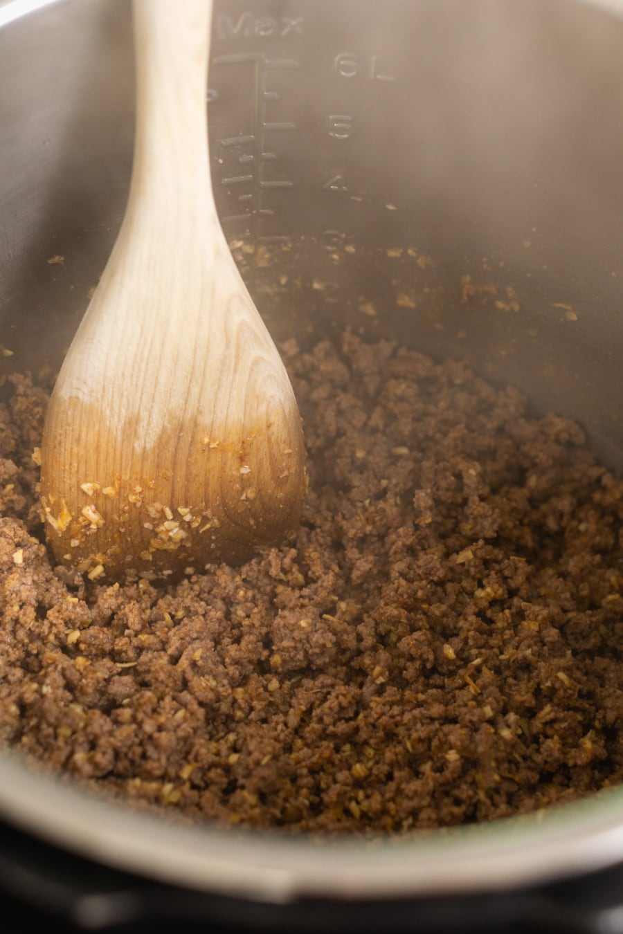 two pounds of seasoned cooked ground beef in the instant pot with a wooden spatula