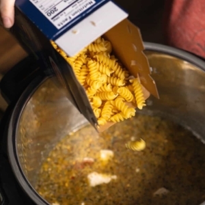 adding rotini pasta to the instant pot for tuscan chicken pasta