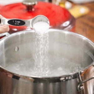 adding salt to a large pot of hot water